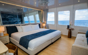 King bed next to mirror wall & 3 large windows looking out to the Galapagos waters in Golden Stateroom aboard Monique yacht.