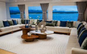 Lounge on small yacht Monique with cream-colored wraparound sofa, accent pillows, modern wood coffee tables & panoramic windows