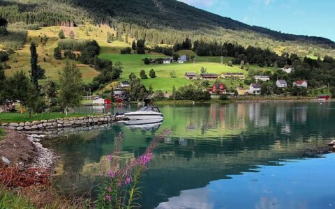 Small white day boat sits docked in glassy water beside rolling green hills during a Norwegian fjords cruise.