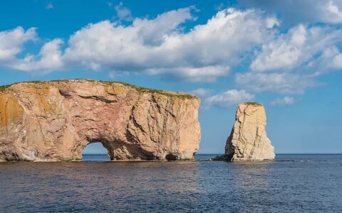Perce's beige rocky outcrop with arch & detached islet over the sea, seen on small boat cruises on the St. Lawrence River.