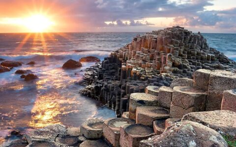 Sunset over the sea by tan circular rock columns on shore, seen on the Treasures of Ireland & The British Archipelagoes trip.