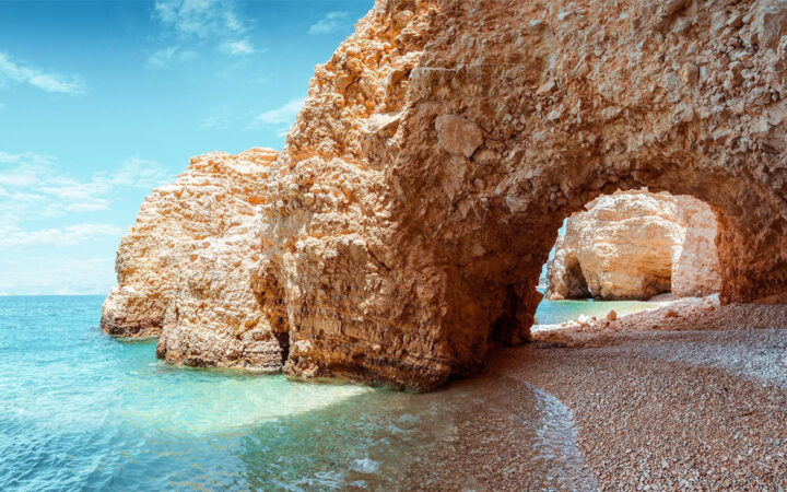 Greece off the beaten path leads to the arch on Kasteli Beach seen with turquoise water and clay-like rock caves.