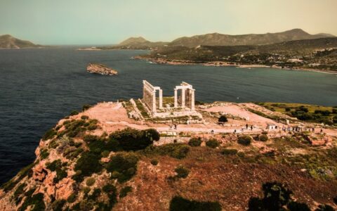 A Greek temple seen from an aerial drone view with ocean and mountains in the background
