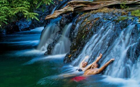 two travelers relax against a rock while water flows over it in the jungle of Corcovado National Park, Costa Rica