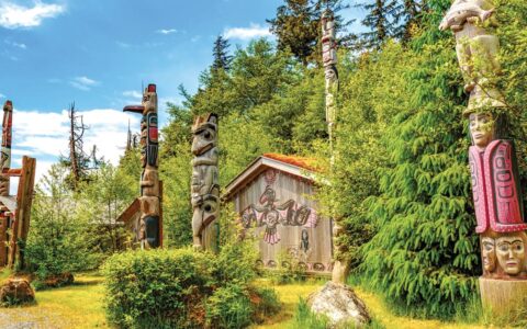 Native American Totems and Clan Houses in Ketchikan, Alaska, set against bright green forest and blue sky.