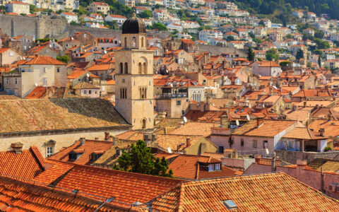 Aerial view of terracotta roofs & a belltower along the hilly old-world city of Dubrovnik, Croatia.