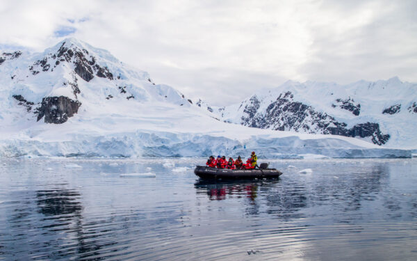 zodiac filled with explorers navigating Antarctica's icy waters in front of snowy white mountains