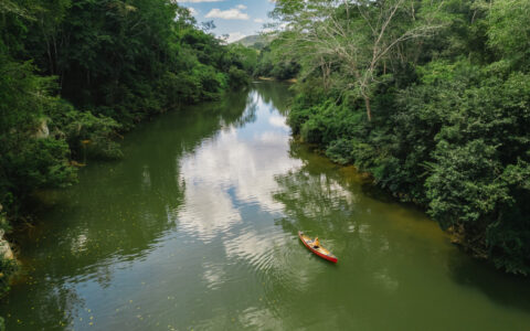 Aerial view of person paddling a red canoe down a glassy river on a Belize jungle tour at Chaa Creek.