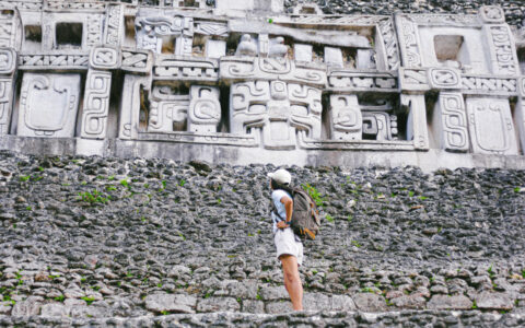 Woman on a Belize jungle tour via Chaa Creek stands on stone steps & looks up at white Aztec stone carvings.