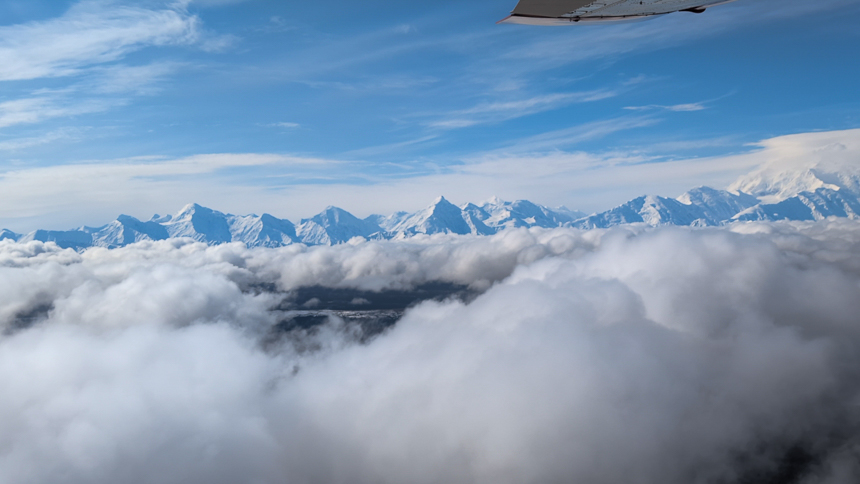 View out of small plane of mountain range in Alaska with snow covered mountains popping through the white clouds