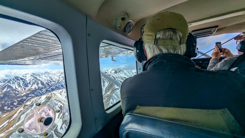 views from inside small airplane overlooking snowy mountain ranges as passengers take pictures 