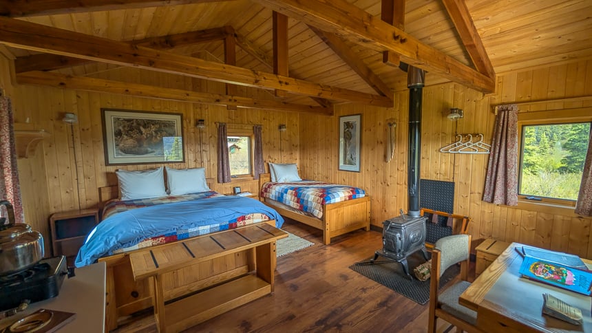 Inside of cabin with a double bed and a twin bed with wood pannels and a small fireplace