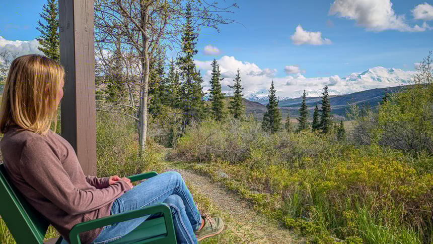 Women sitting in rocking chair overlooking Denali national park with mt Denali covered in snow in the back ground 