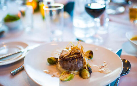 A steak dinner beautifully plated with brussel sprouts on a white place setting