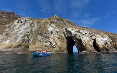 An inflatable zodiac boat filled with travelers in life jackets navigates the waters and rock formations around San Cristóbal Island