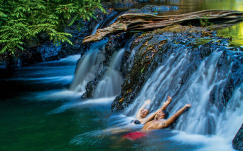 two travelers relax against a rock while water flows over it in the jungle of Corcovado National Park, Costa Rica