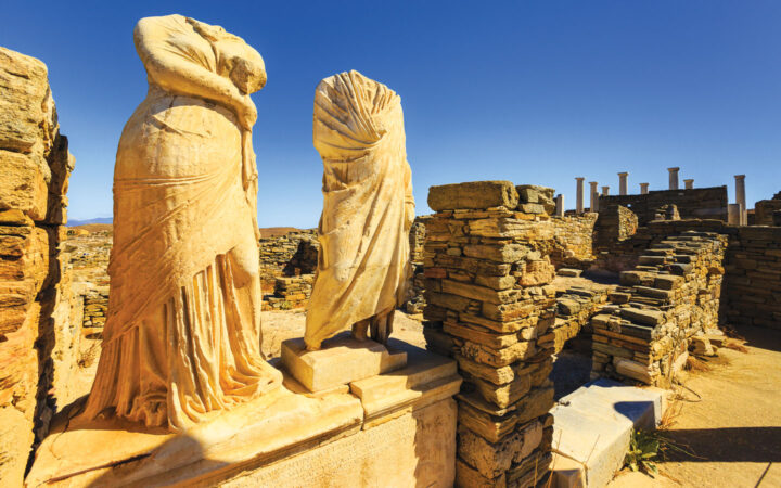 Headless male & female statues in Delos shine golden in sun during a Greece and Turkey cruise.