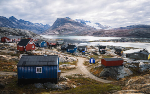 Small coastal town with colorful buildings, green tundra & bare rock under cloudy skies in southeast Greenland.