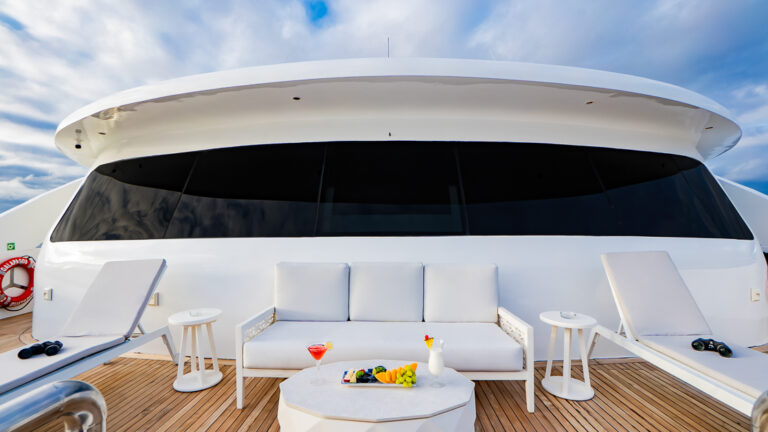 2 wood chaise loungers with blue pads & small green couch with wood coffee table on teak deck of Endemic cruise ship in Galapagos.