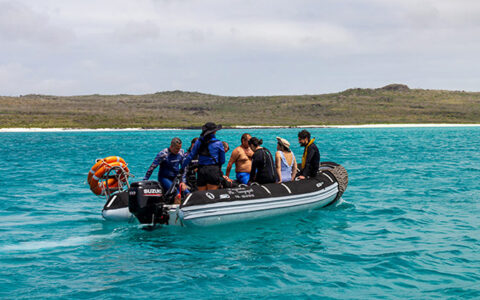 Galapagos Angel cruise passengers seen in a skiff in aqua blue water near a deserted shore