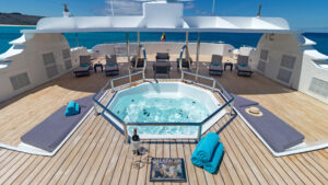 Sun deck of Galapagos Horizon ship with Jacuzzi, chaise loungers with dark blue pads & teak decking.