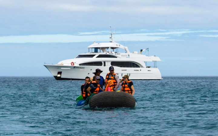 Panga boat with Grand Majestic Galapagos travelers in life jackets motors away from the ship on a sunny day with calm seas.