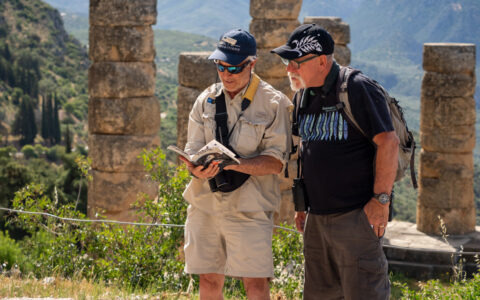 Traveler & guide read a reference book while standing near ancient stone columns on a cruise in Greece, Croatia & Albania.