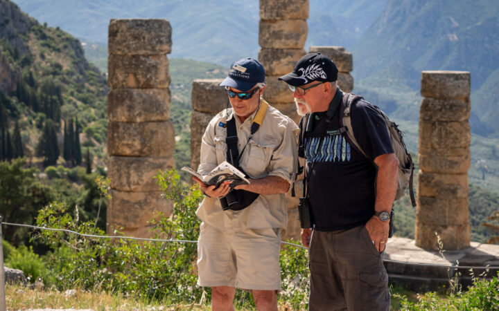 Traveler & guide read a reference book while standing near ancient stone columns on a cruise in Greece, Croatia & Albania.