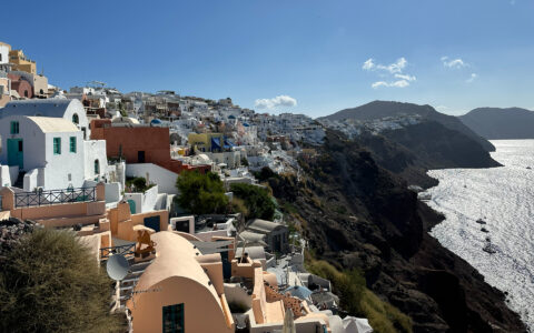 Cliffs of Santorini with stone buildings of varying colors overlooking brightly lit sea, seen on a Greek Isles Odyssey cruise.