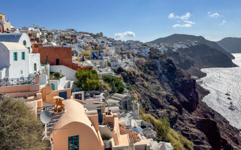 Cliffs of Santorini with stone buildings of varying colors overlooking brightly lit sea, seen on a Greek Isles Odyssey cruise.