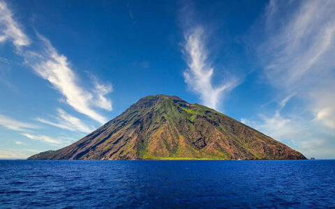 Landscape view of active volcano touring high into the blue skys over the bright blue sea on a calm day