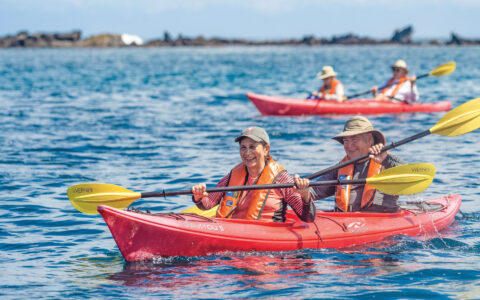 Guests on a Nat Geo Galapagos by Catamaran cruise explore the Buccaneer Cove in tandem red kayaks at Santiago Island.