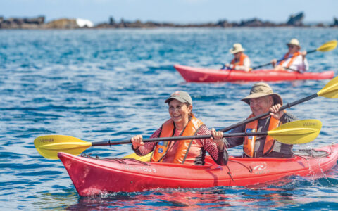Guests on a Nat Geo Galapagos by Catamaran cruise explore the Buccaneer Cove in tandem red kayaks at Santiago Island.