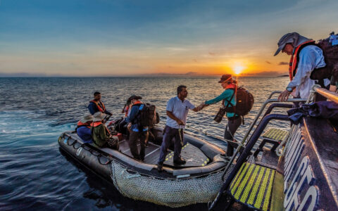 Guests departing a small ship cruise on a skiff with an orange sunset