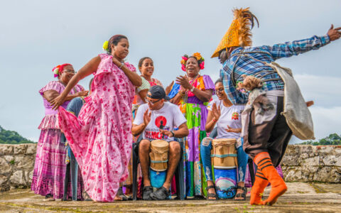 Local dancers in bright, multicolored clothes perform atop a rocky old fort on a Panama Canal, Pearl Islands & Darien Jungle cruise.
