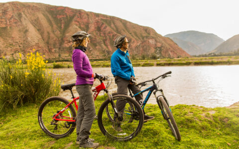 Couple on mountain bikes looking out into the distance overlooking a small lake on a warm sunny day next ti the mounatins