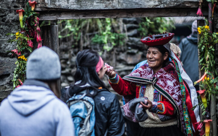 Women in tradtional peru outfit greeting travelers as they enter the scared valley next to the stone walls and flowers all around