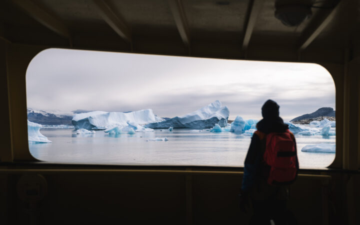 West Greenland traveler on the Disko Bay to Uummannaq cruise stands on deck of ship & views blue icebergs.