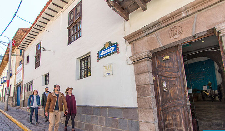 Peru travelers walk a city street to the front of XO Art House in Cusco, with a dark brown wood door & stone facade.