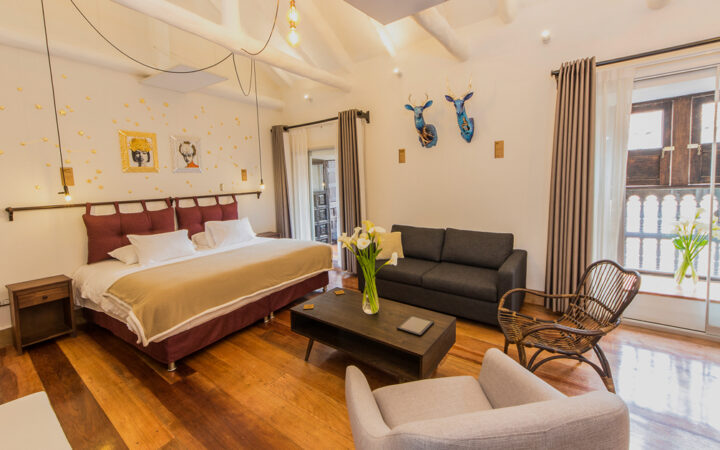 Superior Deluxe room at XO Art House Cusco with king bed, chair & love seat, coffee table, wood floor, large windows & local art.