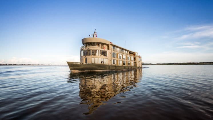 Exterior of bow and port side of Delfin III riverboat at rest in calm water under blue sky during an Amazon River cruise.