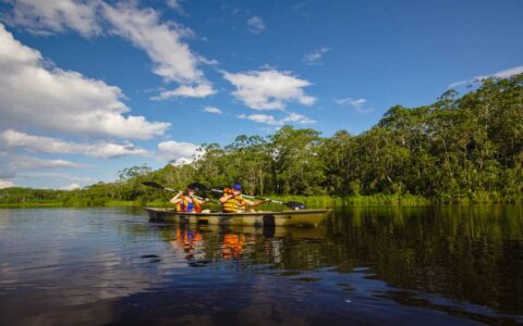 group of adventure travelers in a small motorized boat cruising down the amazon on a calm sunny day with the jungle in the background