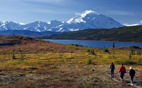 three hikers on trail near lake, mountains on alaska coast to denali journey land tour