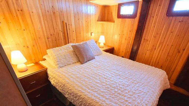 Cabin on Alaska Quest boat with queen bed in white linens, wood-paneled walls, bedside tables & 2 portholes.