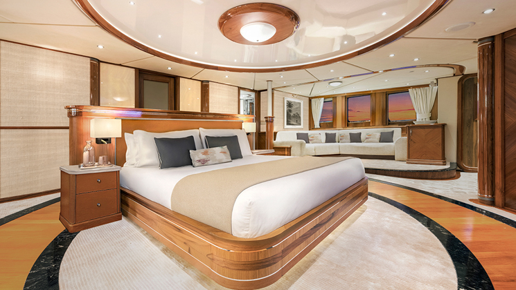 Owner's Suite #303 on Aqua Lares ship with double bed in center of cabin, marble & wood accents, white couch & view windows.