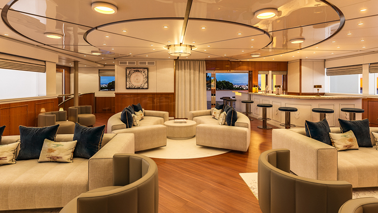 Indoor lounge of Aqua Lares boat in Africa with mid-century modern beige & olive green couches & chairs, marble bar & view windows.
