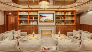 Main saloon on Aqua Lares Africa yacht with wrapround beige couches, marble coffee tables, flit fireplace & wood bookshelves.