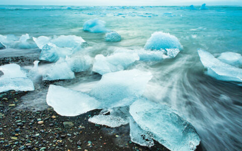 Sheets of crystal teal ice wash ashore to a black sand beach in Iceland seen aboard Wild Iceland Escape Arctic cruise.