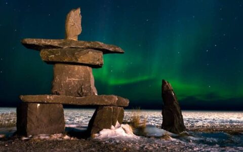 A rock statue in Churchill, Canada with green northern lights shining.