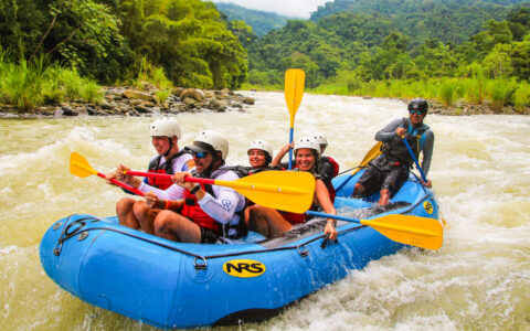 Kontiki Pura Vida Expedition Cruise guests paddle an inflatable blue raft through whitewater rapids beside bright green jungle.